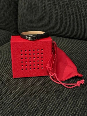 Svart läderarmband från Diesel - Snyggt svart armband i läder från Diesel med ett silverfärgat metallspänne som har märkets logga. Armbandet är stilrent och justerbart, Kommer med röd presentask och tygpåse. Nypris runt 1000 kr