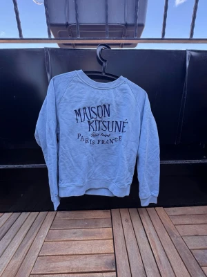 Ljusblå sweatshirt Maison Kitsuné🙌🤩 - Säljer en ljusblå sweatshirt från Maison Kitsuné med tryck i svart och vitt på bröstet där det står 'Maison Kitsuné Paris France'. Tröjan har rund halsringning, långa ärmar och ribbade muddar vid ärmslut och nederkant. Perfekt för en avslappnad och trendig look. I storlek S och har en slim passform🙌🤩