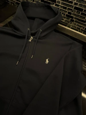 Mörkblå hoodie från Polo Ralph Lauren - Snygg mörkblå hoodie med dragkedja från Polo Ralph Lauren. Klassisk design med huva. Perfekt för en avslappnad och stilren look.