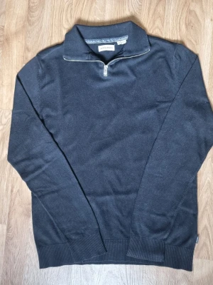 Svart halvzip tröja Jack & Jones - Snygg svart tröja från Jack & Jones med halvzip och hög krage. Tillverkad i mjukt material och har ribbade muddar vid ärmslut och nederkant. Perfekt för en stilren och enkel look.