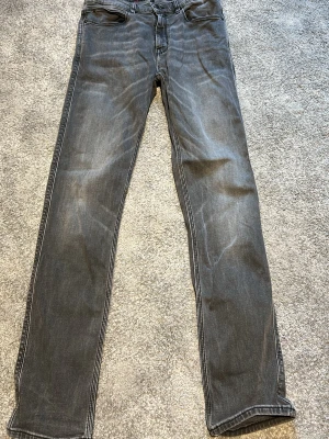 Grå raka jeans med kontrastsömmar - Säljer ett par grå jeans med raka ben och tydliga kontrastsömmar. Jeansen har klassisk femficksmodell och en diskret tvättad look. Perfekta för en avslappnad stil och passar till det mesta. Materialet är mjukt denim i bomull.