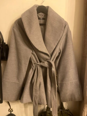 Grå kappa med knytskärp - Stilren grå kappa från bikbok med bred krage och knytskärp i midjan. 