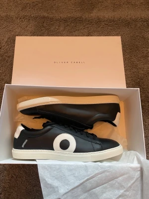 Svarta sneakers från Oliver Cabell - Sprillans nya svarta sneakers från Oliver Cabell i läder med vit sula och vit detalj på sidan. Skorna har svarta skosnören. Hör av er vid frågor eller funderingar 