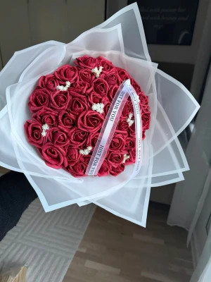 Bukett med röda konstrosor - Säljer en bukett med röda konstgjorda rosor inslagna i vitt papper och dekorerad med små vita blommor. Buketten har ett band med texten 'Just for you' och passar perfekt som present eller dekoration.