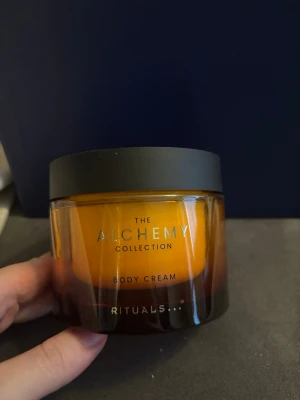 Rituals The Alchemy Body Cream - Lyxig body cream från Rituals The Alchemy Collection i en snygg bärnstensfärgad burk med svart lock. Krämig formula som återfuktar huden och ger en mjuk känsla. Perfekt för dig som vill ha en exklusiv kroppsvård med elegant design.