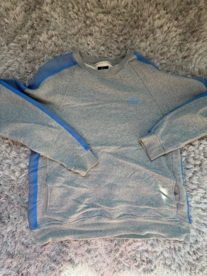 Needles Grå Blå Striped Tröja Med Brodyr Storlek M - Säljer denna snygga clean Needles japanska tröjan. Den har broderade stripes på sidan och broderad logga på framsidan, och hidden fickor. Riktigt skön casual tröja för den som gillar unik streetwear. Använd några gånger men helt felfri. Rekommenderas starkt!