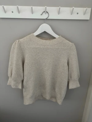 Beige stickad tröja med puffärm - Säljer en beige stickad tröja med puffärm och ribbade muddar. Tröjan är lite nopprig men inget som förstör.  Passar dig som gillar en enkel men trendig look.