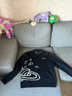 Svart stickad tröja från broken planet - Snygg svart stickad tröja från broken planet med vita grafiska mönster och stjärnor både fram och bak. Tröjan har rund halsringning och långa ärmar. Perfekt för dig som gillar streetwear och unik design.