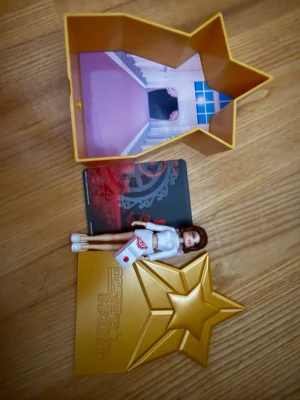 Dress to Impress docka (secret) (utan dlc kod) - Säljer en liten docka med brunt hår, vit topp och kjol samt ett litet brev i handen. Medföljer en guldig stjärnformad ask med inredning som ser ut som ett rum och en dekorativ kortbit. Perfekt för samlare eller som leksak. Dress to impress docka, en av de ”secret” dockorna, utan DLC kod.