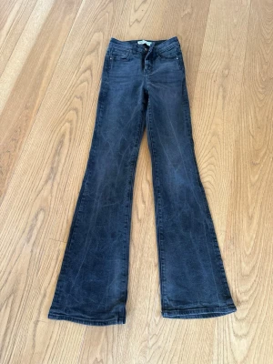 Svarta bootcut jeans med utsvängda ben mörkgrå zara - Snygga svarta / mörkgrå bootcut jeans med utsvängda ben och klassisk femficksdesign. Jeansen har en hög midja och är tillverkade i stretchigt denimtyg för extra komfort. Perfekta för dig som gillar en retroinspirerad look. Från Zara storlek 32.