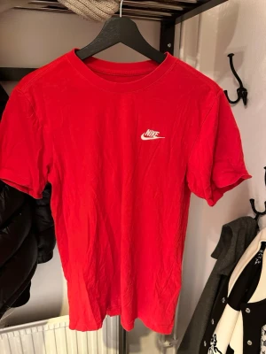 Röd Nike t-shirt med logga - Säljer en klassisk röd t-shirt från Nike med vit logga på bröstet. T-shirten har rund hals och korta ärmar, perfekt för dig som gillar sportiga och stilrena plagg. Materialet är mjuk bomull som känns skönt mot huden.