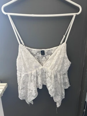 Vit spetsig linnetopp  - Säljer en söt vit linnetopp med tunna axelband och v-ringad hals. Toppen är täckt av spets och är pösig nedtill som ger en luftig känsla. Perfekt för varma dagar eller sommarens alla tillfällen.