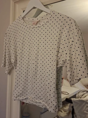 Vit prickig t-shirt från Gina Tricot - Säljer en vit t-shirt från Gina Tricot med svarta prickar över hela plagget. Klassisk rund halsringning och korta ärmar och tajt i midjan.