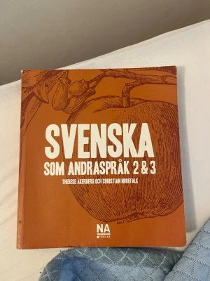 Svenska som andraspråk 2 & 3 bok - Lärobok i svenska som andraspråk för kurserna 2 och 3, skriven av Therese Åkerberg och Christian Norefalk. Boken har ett brunt omslag med ett stort äpple i tecknad stil och tydlig vit text. Perfekt för gymnasiet eller vuxenutbildning.