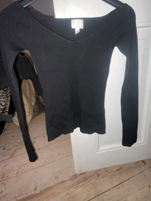 Svart ribbad v-ringad topp H&M - Säljer en svart ribbad topp från H&M i storlek XS. Toppen har v-ringning och långa ärmar, perfekt för att styla med jeans eller kjol. Materialet är mjukt och stretchigt för en bekväm passform.