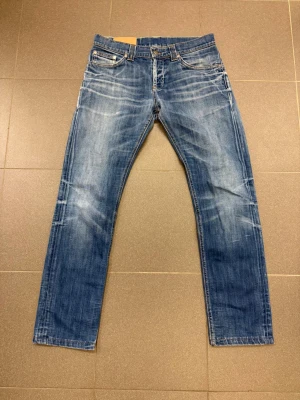 Dondup Blå raka jeans Slim fit  - Säljer ett par klassiska blå jeans från Dondup med raka ben och snyggt slitna detaljer. Jeansen har fem fickor, orange sömmar och är gjorda i mjuk denim. Perfekta för en avslappnad och trendig stil.