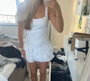 Vit kort volangklänning  - Superfin vit kort klänning med volangkjol och inbyggda shorts. Klänningen har en figurnära passform och är perfekt för sommarens alla tillfällen. Snygg och enkel design som känns både trendig och söt.