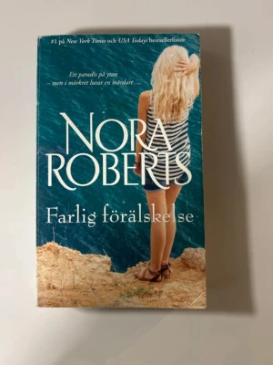 Farlig förälskelse av Nora Roberts - En spännande pocketbok av Nora Roberts, 'Farlig förälskelse', med ett omslag i blått och beige. Boken handlar om mysterier och romantik på mexikanska Cozumel. Perfekt för dig som gillar romantik och spänning.