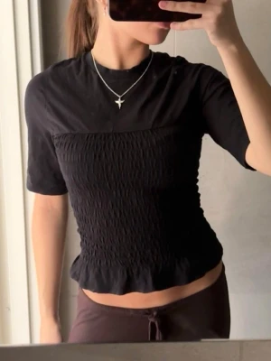 Svart ribbad topp med volangkant - Säljer en svart topp med ribbad, smockad midja och volangkant nedtill💕Snygg tshirt med detalj. Från H&M