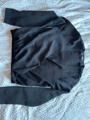 Svart omlottopp med långa ärmar - Snygg svart omlottopp från NA-KD med långa ärmar och v-ringad hals. Toppen har en elegant omlottdesign och är tillverkad i ett mjukt, slätt material som ger en stilren look. Perfekt att matcha med både jeans och kjol för en trendig outfit. ALDRIG ANVÖND