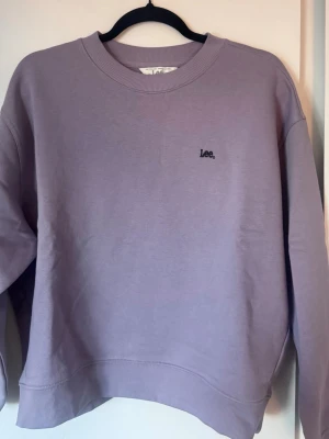 Ljuslila sweatshirt från Lee - Helt oanvänd. Så matrerialet är precis som nytt!En stilren ljuslila sweatshirt från Lee med diskret logga broderad på bröstet. Tröjan har rund halsringning, ribbade muddar vid ärmslut och nederkant samt en avslappnad passform. Perfekt för en chill och trendig look.😊 nypris 400