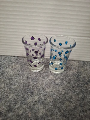 Två shotglas med leopard mönster - Säljer två små shotglas i klart glas, ett dekorerat med lila prickar och ett med blå prickar. Glasen har en klassisk form med lätt utsvängd kant och är perfekta för shots eller små drinkar. Unika och lekfulla detaljer som sticker ut på festen.