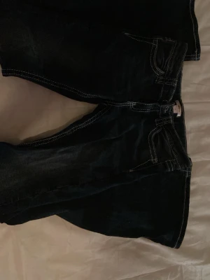 Mörkblåa utsvängda jeans med låg midja  - Säljer ett par mörkblå jeans med kontrastsömmar och unika broderade bakfickor med mönster och detaljer. Klassisk femficksmodell och raka ben. Perfekta för dig som vill ha något extra i din denimlook.