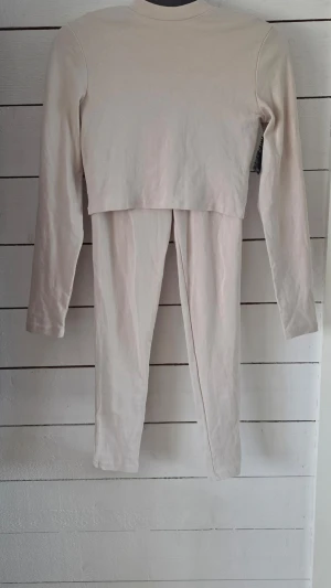 Beige långärmat bodyset - Säljer ett stilrent beige bodyset med långärmad topp och matchande byxa. Setet har en enkel, tight passform och är tillverkat i mjukt bomullsliknande material. Perfekt för dig som gillar minimalistisk och clean stil.