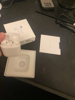 Apple AirPods gen 2 - Säljer ett par vita Apple AirPods med tillhörande laddningsetui. Snygg och stilren design i blank plast, perfekt för dig som vill ha trådlösa hörlurar till mobilen. Kommer med originalförpackning och manual.