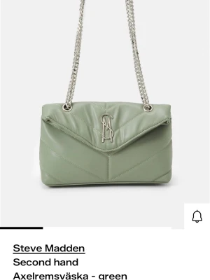 Grön axelväska från Steve Madden - Snygg ljusgrön axelväska från Steve Madden med quiltad design och silverfärgad kedjerem. Väskan har ett stort metallogo framtill och v-format lock. Tillverkad i konstläder som ger en trendig look.