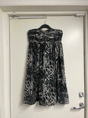 Axelbandslös klänning med leopardmönster - Säljer en axelbandslös klänning i svart, grått och vitt med leopard- och zebramönster. Klänningen har en vid kjol och smockad överdel som ger en snygg passform. 