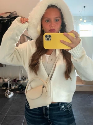 Vit teddyjacka med huva - Mysig vit teddyjacka med fluffig huva och dragkedja framtill. Jackan är croppad och har ribbade muddar vid ärmslut och midja. Perfekt för dig som gillar en avslappnad och trendig stil.