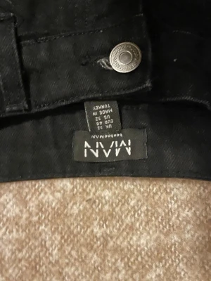 Svarta jeans med slitningar från MAN - Säljer ett par svarta jeans från MAN med unika slitningar och patchade detaljer på benen. Jeansen har raka ben och klassisk femficksmodell. Materialet är denim och de har en cool, edgy look som sticker ut.