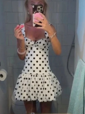 Vit prickig klänning från zara - Supersöt vit kort klänning med svarta prickar och breda axelband. Klänningen har en liten rosettdetalj framtill och en volangig kjol som ger en lekfull look. Perfekt för varma dagar och somriga vibes.