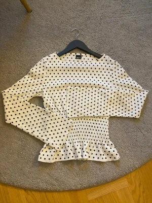 Vit prickig blus - Supersöt vit blus från Gina Tricot med svarta prickar, smockad midja och volangkant nedtill. använt en gång så den är som ny. !Skriv om ni vill se den på!💞
