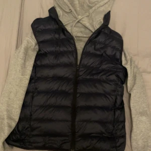Uniqlo väst - Säljer en marinblå dunväst från Uniqlo Ultra Light Down-kollektionen. Västen är lätt, quiltad och har dragkedja framtill. Perfekt att slänga över en hoodie för en avslappnad och stilren look. Tillverkad i lätt och smidigt material som håller värmen.