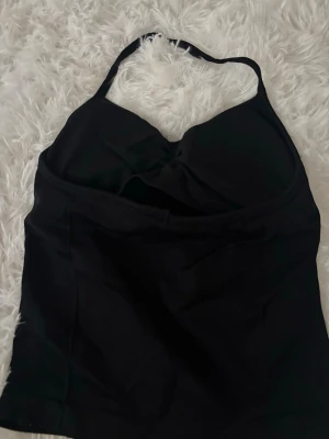 Svart halterneck topp  - Snygg svart topp med halterneck och vadderade kupor. Klassisk modell med enkel design och mjukt stretchigt material som formar sig efter kroppen. Perfekt för gymmet 