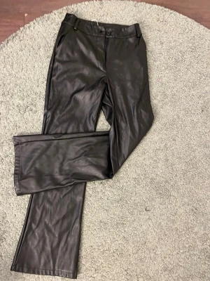 Svarta fuskskinnbyxor bootcut - Snygga svarta byxor i fuskskinn med bootcut-modell från madlady. Byxorna har knapp och dragkedja framtill samt bälteshällor. Perfekta för dig som vill ha en trendig och edgy look.