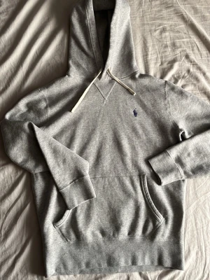 Grå äkta hoodie från Polo Ralph Lauren - Snygg grå hoodie från Polo Ralph Lauren med klassisk huva och vit dragsko. Diskret blå logga broderad på bröstet och praktisk magficka. Långa ärmar och ribbade muddar för extra komfort. Lägg gärna bud och skicka om ni vill ha någonnytterligare bild eller om ni har någon fråga. Har rl tagsen också om man vill att jag ska ta bild på dem.