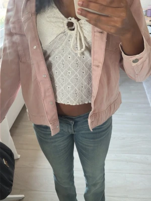 Ljusrosa jeansjacka i klassisk modell - Trendig ljusrosa jeansjacka med silverfärgade knappar och raka sömmar. Jackan har klassisk krage, bröstfickor och är tillverkad i ett mjukt jeanstyg. Perfekt att slänga över en topp för en avslappnad look.