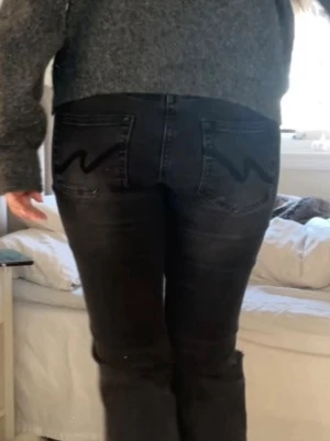 Svarta bootcut jeans med hål - Säljer ett par svarta bootcut jeans med slitna hål på båda knäna och klassiska bakfickor med vågig söm. Jeansen har låg midja och är i stretchigt denimtyg, perfekta för en avslappnad och trendig look. Obs: jag har sprättat upp dom så att de ska bli längre som man ser på bild 2!💕