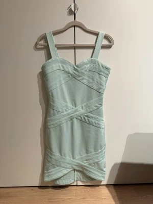 Ljusgrön kort klänning  - Snygg ljusgrön kort klänning med breda axelband och korsade detaljer framtill. Klänningen har en figurnära passform och dragkedja i ryggen. 