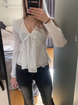Vit volangblus med v-ringning - Söt vit blus med v-ringning och volangdetaljer från Gina Young i storlek 158/164. Materialet är tunt och luftigt, perfekt inför våren och sommaren. Fint skick, då jag inte använt den så mycket 