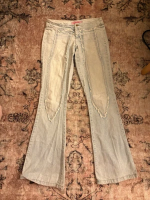 Ljusblå bootcut jeans med detaljer - Unika ljusblå jeans med bootcut passform och råa, dekorativa sömmar framtill. Jeansen har en retroinspirerad look med breda ben och markerade paneler. Perfekta för dig som vill sticka ut med en cool vintage vibe. har ett hål men man kan inte se när man ha på !!!