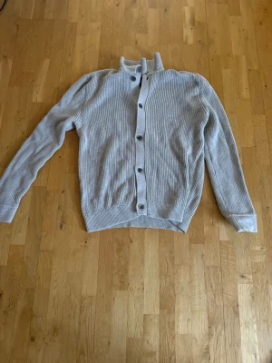  ribbad kofta från Bondelid - Beige ribbstickad kofta från Bondelid med knappar framtill och hög krage. Koftan har långa ärmar och breda muddar vid ärmslut och nederkant. Ny pris 899kr