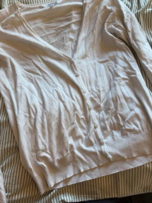 Vit kofta från BASICU med knappar - Klassisk vit kofta från BASICU i storlek L (44/46) men passar även S/M då den är liten i storleken. Koftan har v-ringning, långa ärmar och stängs med matchande vita knappar framtill. Tillverkad i ett tunt, mjukt material som passar perfekt till lager på lager och vardagslooken. 