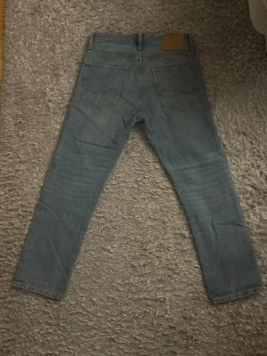 Ljusblå raka jeans från Jack and Jones - Säljer ett par ljusblå raka jeans från Jack and Jones med klassisk femficksdesign och raka ben. Jeansen har en snygg tvättad look och är tillverkade i bomull. Perfekt för dig som gillar en enkel och stilren jeansstil.
