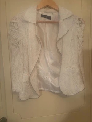 Vit spetsjacka från Sisters Point - Säljer en vit jacka från Sisters Point med vackra spetsdetaljer och öppen framsida. Jackan har långärmade ärmar med voluminös effekt och ett elegant, figurnära snitt. Perfekt för dig som vill ha en unik och stilren look.