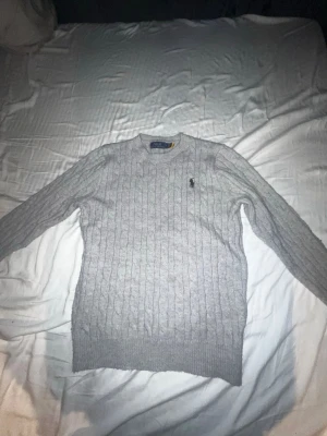 Ljusgrå kabelstickad tröja Polo Ralph Lauren - Säljer en ljusgrå kabelstickad tröja från Polo Ralph Lauren. Tröjan har rund halsringning, lång ärm och den klassiska broderade loggan på bröstet. Tillverkad i mjukt material som passar perfekt till lager på lager under kyliga dagar. priset kan diskuteras 