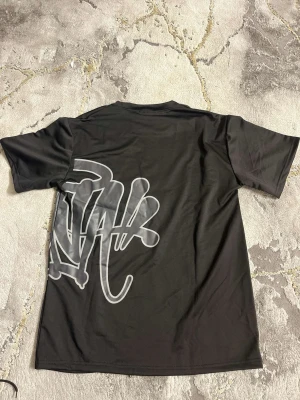 Svart t-shirt med stor grafisk print - Svart t-shirt från Lifewear med stor, vit grafisk print som sträcker sig från framsidan till baksidan. T-shirten har rund halsringning och korta ärmar. Materialet känns mjukt och lätt, perfekt för en avslappnad stil.
